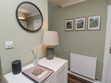 A hallway with a round mirror a table lamp a small cabinet and three framed pictures above a radiator at Sparrow House in Alnwick