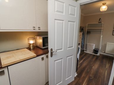 A utility room with a microwave lamp and cutting board on the counter a washing machine laundry basket and ironing board at Sparrow House in Alnwick