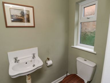 A bathroom with a white sink and toilet with wooden toilet seat under a window at Sparrow House in Alnwick