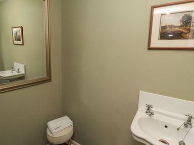 A bathroom with a white sink a round stool with folded towels a large mirror and framed pictures on the wall at Sparrow House in Alnwick