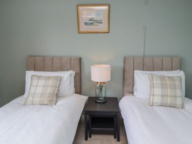 A bedroom with two single beds a nightstand with a lamp and a framed picture on the wall at Sparrow House in Alnwick