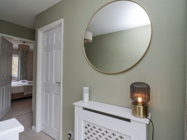 A hallway with a round mirror above a white radiator cover and a bedroom visible through an open door at Sparrow House in Alnwick