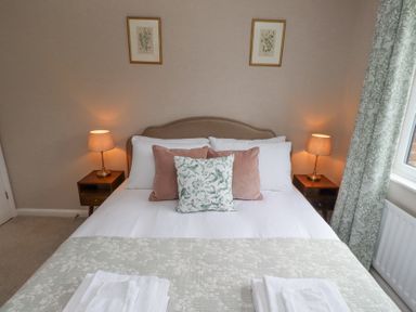 A bedroom with a double bed two side tables with lamps two framed pictures on the wall and patterned curtains at Sparrow House in Alnwick