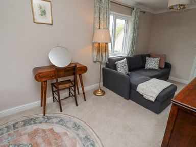 A room with a dark gray sofa and floral cushions a wooden dressing table with a round mirror and chair a floor lamp and a patterned curtain at Sparrow House in Alnwick