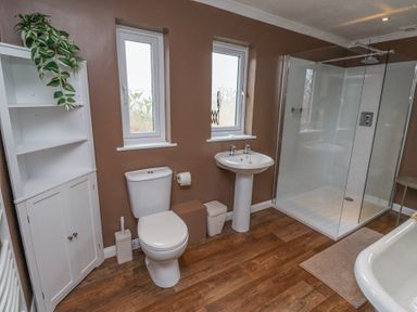 A bathroom with a white toilet, pedestal sink, glass shower enclosure, white cabinet with plant, and wood floor at Sparrow House in Alnwick