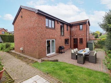 A brick house with a patio dining set and a barbecue grill in a garden at Sparrow House in Alnwick