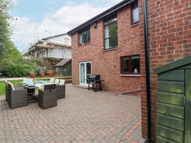 A backyard patio with outdoor dining table and chairs a barbecue grill potted plants and a small green shed at Sparrow House in Alnwick