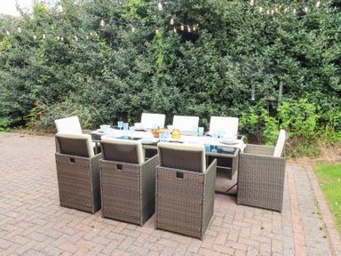 An outdoor dining table with chairs set on a paved patio area with string lights above and bushes behind at Sparrow House in Alnwick
