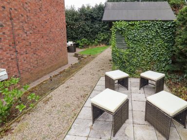 A garden area with four cushioned stools on a tiled patio near a green shed covered in ivy at Sparrow House in Alnwick