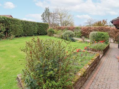 A garden with flower beds and bushes next to a paved pathway at Sparrow House in Alnwick