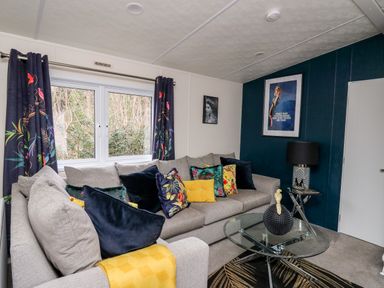 A living room with a grey sofa decorated with colorful cushions and a yellow throw blanket at The Hideout in Gilfachrheda near Llanarth