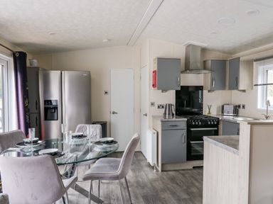 A kitchen area with a dining table set with bowls and glasses next to a refrigerator and stove at The Hideout in Gilfachrheda near Llanarth