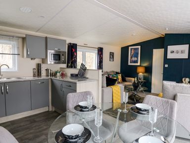 A kitchen and living area with grey cabinets a glass dining table and a sofa at The Hideout in Gilfachrheda near Llanarth