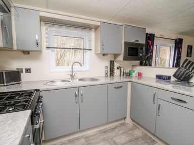 A kitchen with grey cabinets a double sink a gas stove a microwave and a knife set at The Hideout in Gilfachrheda near Llanarth
