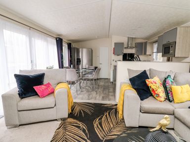 An open living and kitchen area with sofas, a dining table, a refrigerator, and kitchen cabinets at The Hideout in Gilfachrheda near Llanarth