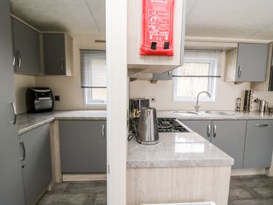 A kitchen with grey cabinets a gas stove a kettle a sink and an air fryer at The Hideout in Gilfachrheda near Llanarth