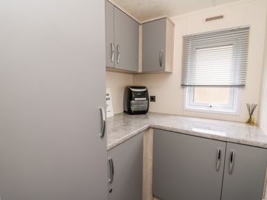 A corner kitchen area with gray cabinets a countertop a small black appliance a window with blinds and a reed diffuser at The Hideout in Gilfachrheda near Llanarth