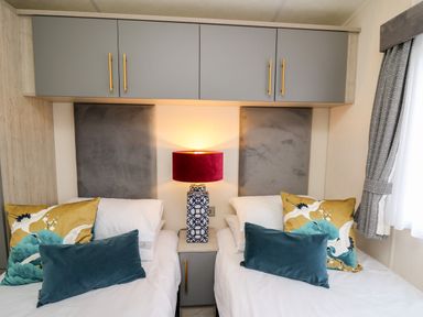 A bedroom with two single beds a bedside table with a lamp above storage cabinets and a window with curtains at The Hideout in Gilfachrheda near Llanarth