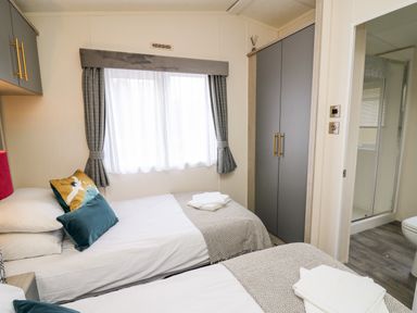 A bedroom with two single beds with pillows and folded towels near a window and a tall wardrobe at The Hideout in Gilfachrheda near Llanarth