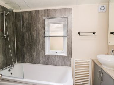 A bathroom with a bathtub shower combination a window with blinds a sink on a countertop and a towel radiator at The Hideout in Gilfachrheda near Llanarth