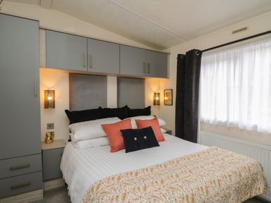A bedroom with a bed with pillows and a floral blanket next to a window with curtains at The Hideout in Gilfachrheda near Llanarth