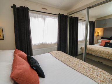A bedroom with a bed with patterned bed runner and cushions next to a window with curtains and mirrored closet doors at The Hideout in Gilfachrheda near Llanarth