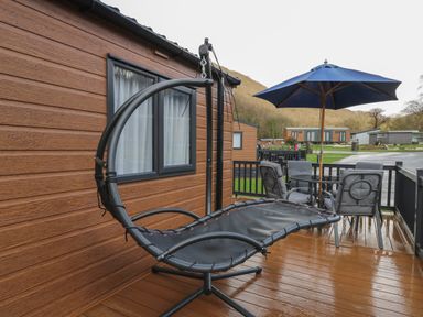 A wooden deck with a hanging chair a patio table with four chairs and a blue umbrella at The Hideout in Gilfachrheda near Llanarth