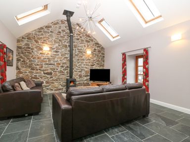 A living room with stone wall wood stove two dark leather sofas skylights and red curtains at The Old Dairy in Sarn Bach near Abersoch