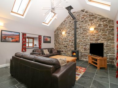 A living room with a stone wall wood burner two brown sofas a coffee table and a television at The Old Dairy Sarn Bach near Abersoch