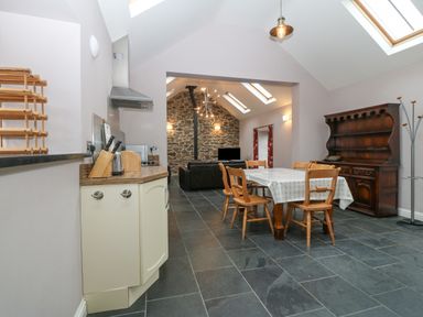 A kitchen area with a dining table and chairs overlooking a living room with a stone wall and skylights at The Old Dairy in Sarn Bach near Abersoch