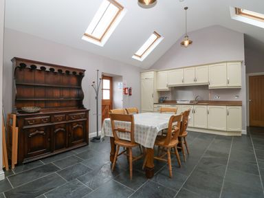 A kitchen with a dining table and chairs a wooden cupboard and cupboards under skylights at The Old Dairy in Sarn Bach near Abersoch
