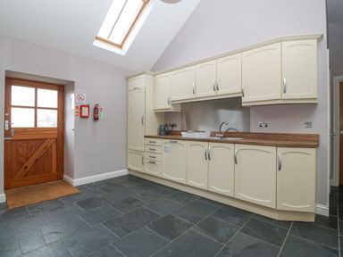 A kitchen with cream cabinets a wooden door and a skylight at The Old Dairy in Sarn Bach near Abersoch
