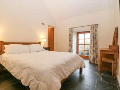A bedroom with a bed white bedding wooden furniture and a window with floral curtains at The Old Dairy in Sarn Bach near Abersoch