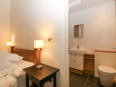 A bedroom with a wooden bed and bedside table with lamp next to a bathroom with a sink mirror and toilet at The Old Dairy in Sarn Bach near Abersoch
