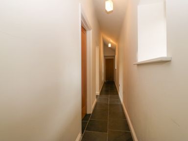 A narrow hallway with tile floor and doors along the sides at The Old Dairy in Sarn Bach near Abersoch