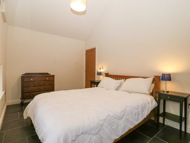 A bedroom with a double bed side tables lamps and a wooden chest of drawers at The Old Dairy in Sarn Bach near Abersoch