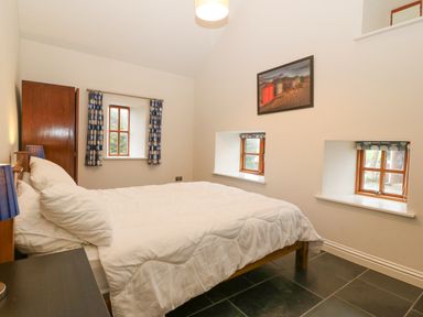 A bedroom with a double bed white bedding wood furniture and three windows at The Old Dairy in Sarn Bach near Abersoch