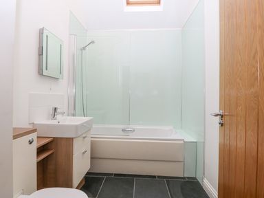 A bathroom with a bathtub shower combo sink and wooden door at The Old Dairy in Sarn Bach near Abersoch