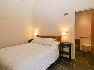 A bedroom with a double bed flanked by two lamps on bedside tables and a door leading to a bathroom at The Old Dairy in Sarn Bach near Abersoch