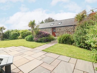 An outdoor garden with a paved patio lawn shrubs and a stone building with a door and skylights at The Old Dairy in Sarn Bach near Abersoch