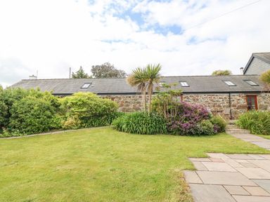 A stone cottage with a grey roof surrounded by bushes flowers and palm trees at The Old Dairy in Sarn Bach near Abersoch