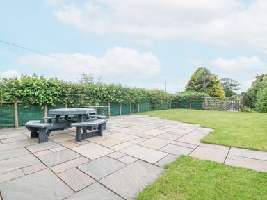 An outdoor patio area with a round picnic table and benches next to a lawn at The Old Dairy in Sarn Bach near Abersoch
