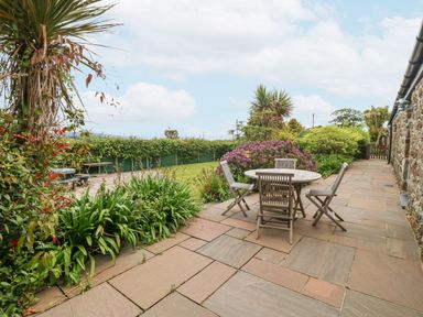 An outdoor patio with a round table and four chairs surrounded by plants and a lawn at The Old Dairy in Sarn Bach near Abersoch