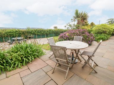 An outdoor patio with a round wooden table and four chairs surrounded by plants and bushes at The Old Dairy in Sarn Bach near Abersoch