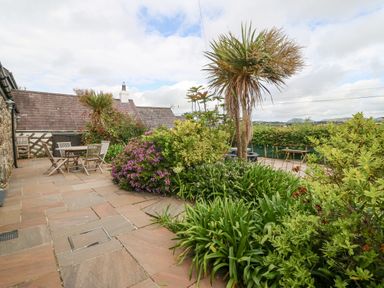 A garden patio area with outdoor tables and chairs surrounded by bushes and plants at The Old Dairy in Sarn Bach near Abersoch