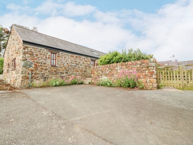 A stone building with small windows and a wooden gate next to a stone wall with flowers at The Old Dairy in Sarn Bach near Abersoch