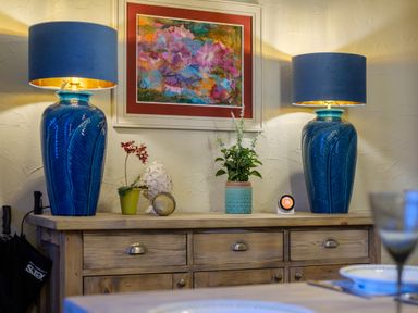 A wooden sideboard with two blue table lamps plants and a colorful painting above at Sunny Brae in Lindale