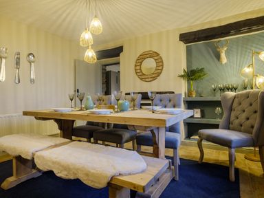 A dining room with a wooden table, upholstered chairs, benches with fur covers, decorative plates, glasses, and wall decor at Sunny Brae in Lindale