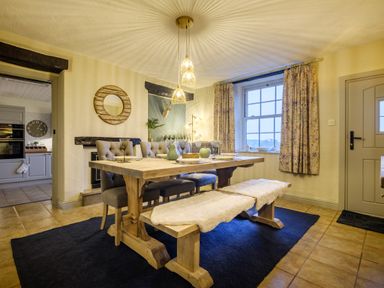 A dining room with a wooden table chairs and a bench a round mirror on the wall and a window with curtains at Sunny Brae in Lindale