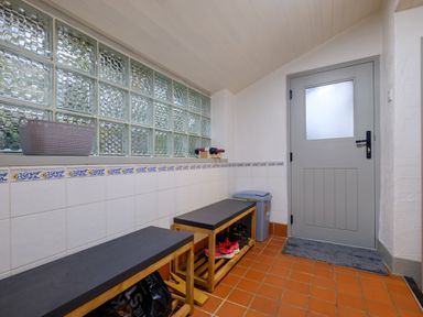 A tiled utility room with two wooden benches with cushions shoes underneath a window with glass blocks and a gray door at Sunny Brae in Lindale